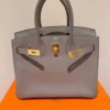 Authentique et neuf, le sac Birkin 30 Hermès couleur Étain doré avec finitions dorées, en cuir Clémence.